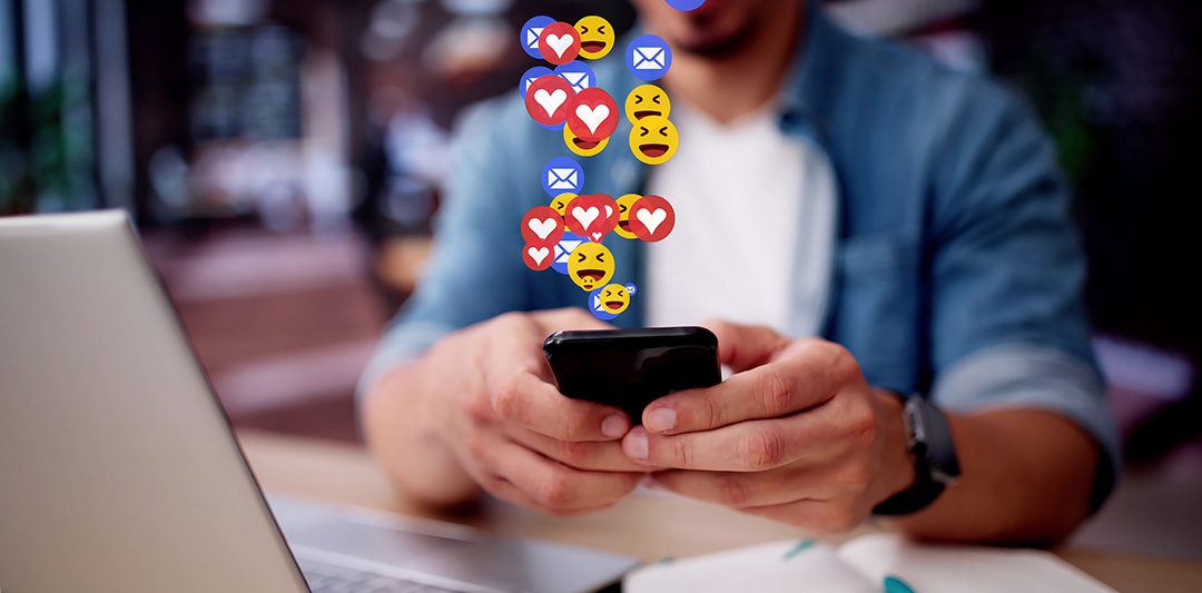 image depicting social media management engagement with hearts and other emoji popping out of a mans phone